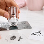 Clear nail stamper picking up a patterned design from a stamping plate beside a BIUTEE nail stamping kit